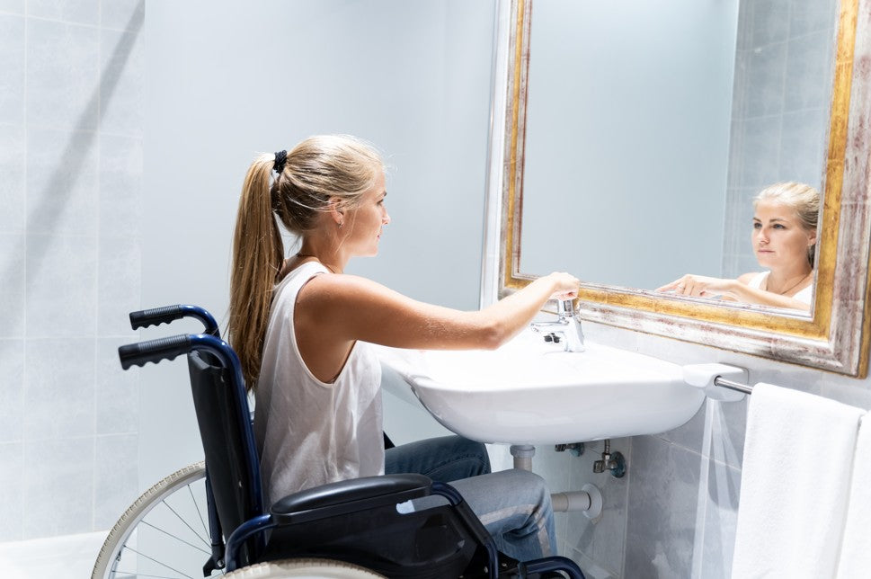 Woman in a wheelchair looking into a mirror in a bathroom.